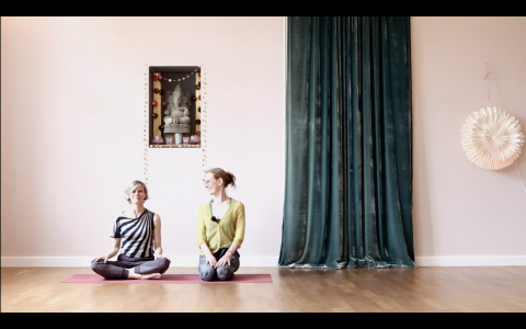 2 Frauen nebeneinander auf 2 Yogamatten. Sie lächeln sich an.