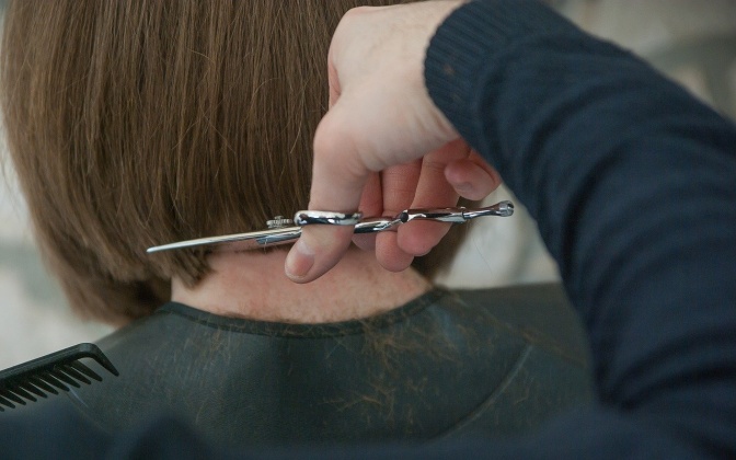 Eine Hand schneidet einer Frau die Haare im Nacken etwa auf Kinnhöhe ab.