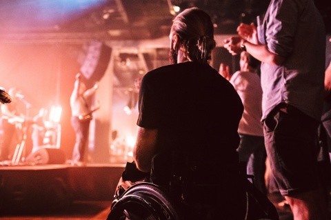 Ein Mann im Rollstuhl hört einem Konzert auf einer Bühne zu.